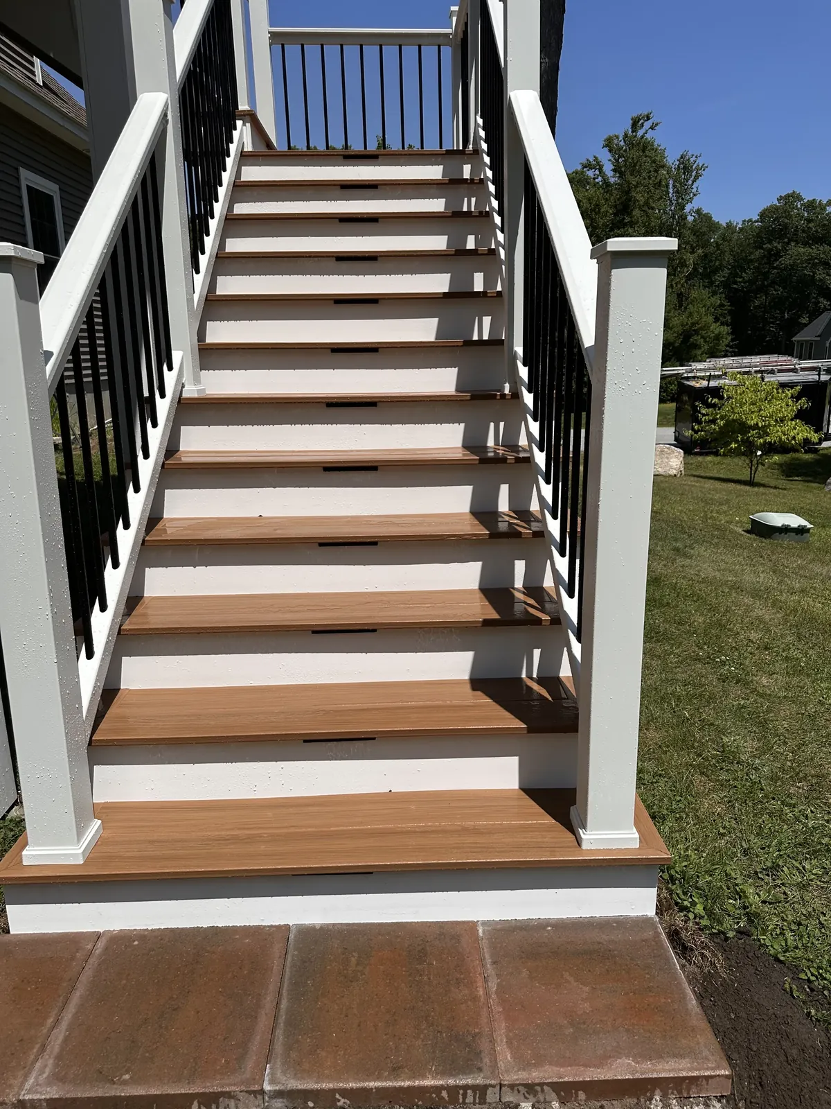 Composite deck stairs with white risers, black aluminum balusters, and recessed riser lights in Kingston, NH