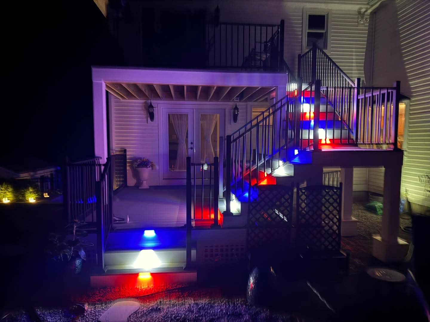 Two-level deck at night with red, white, and blue Truscapes LED riser lighting